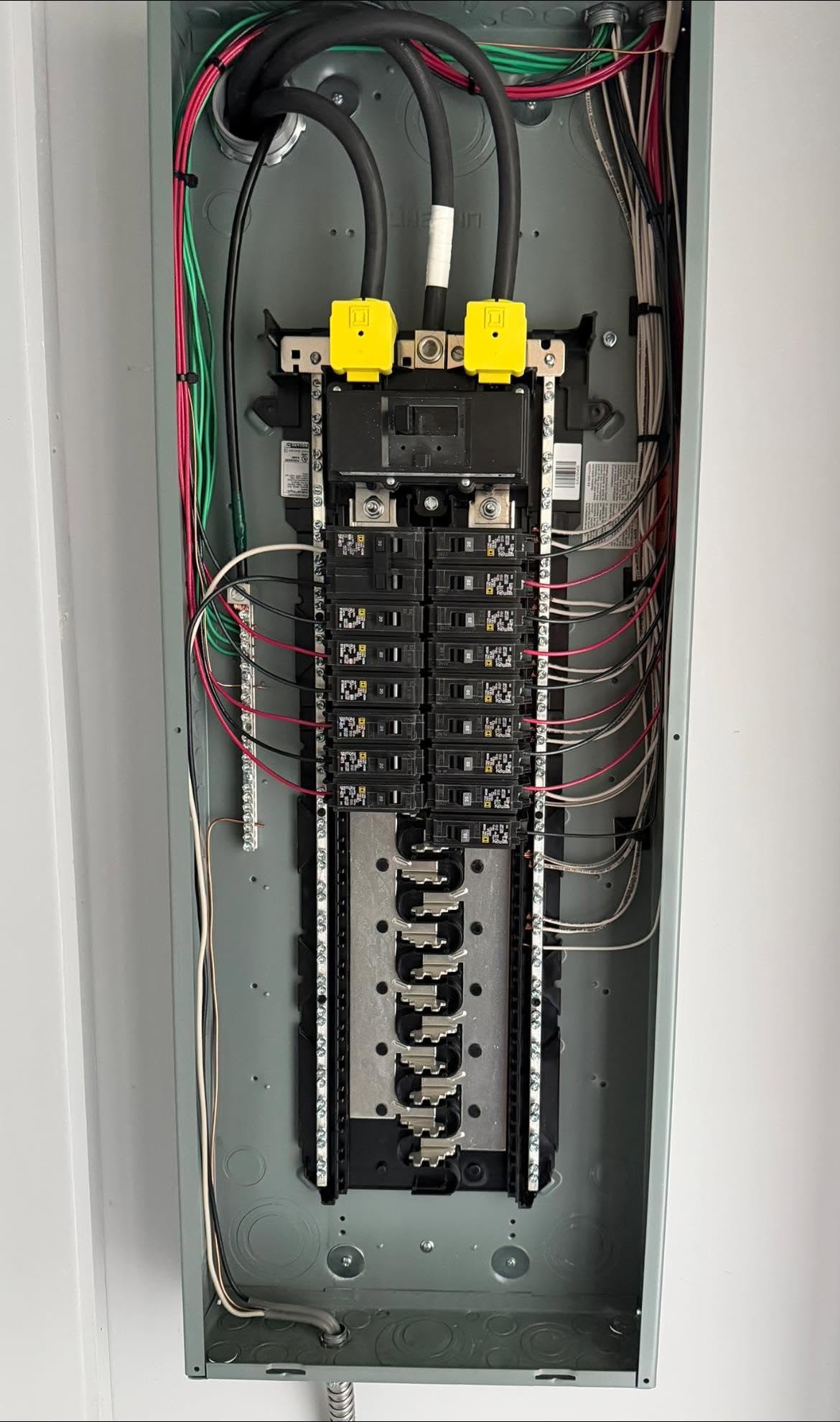 Open electrical breaker panel showing multiple circuit breakers, wiring, and bus bars organized vertically inside a metal enclosure.