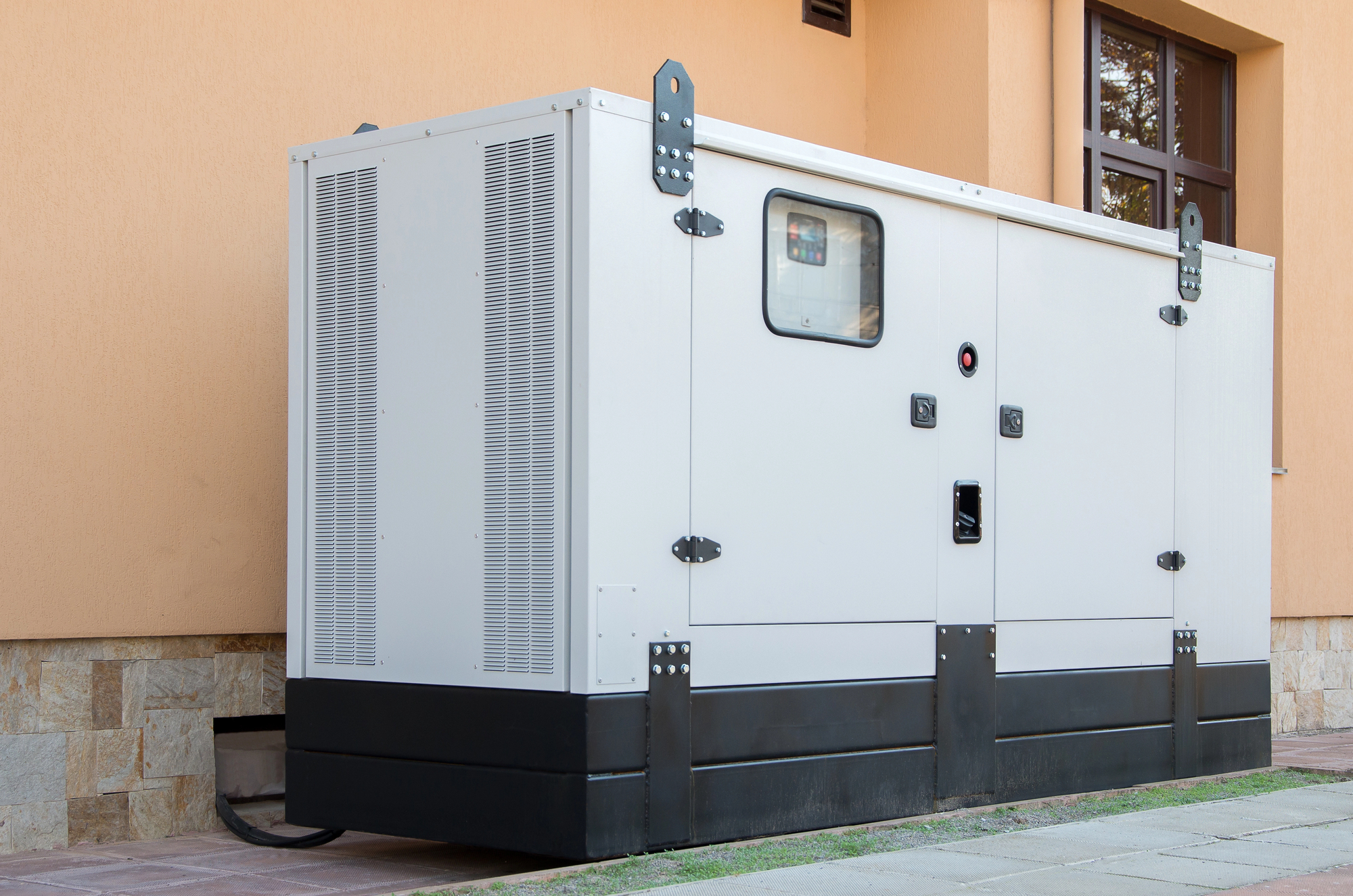 A large, white backup generator is installed outside a building with beige walls and windows.